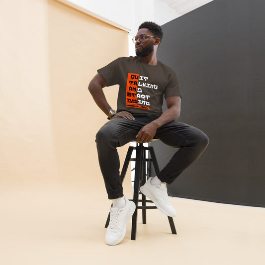 Man sitting on a stool wearing a t-shirt with text, against a plain background